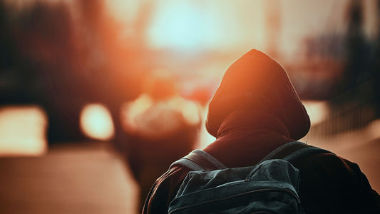 Person carrying a backpack silhouetted against a city skyline at golden hour