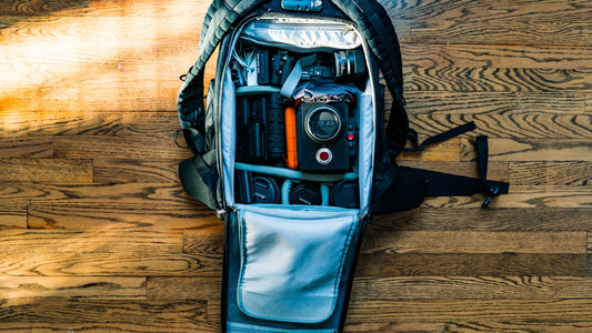 DSLR camera and lens packed inside an open backpack on a wood floor